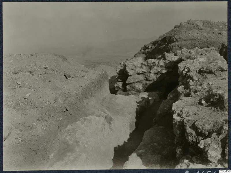 Excavation trench at Vouni Palace cutting between rock and stone masonry, with a hazy view of plains beyond.