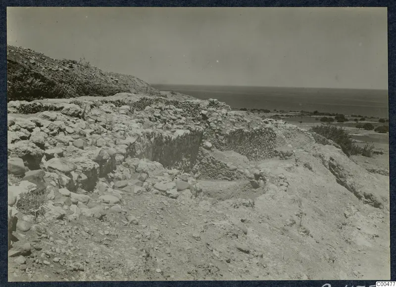 Ruined stone walls on a stony slope at Soli, with a hillside behind and the sea beyond.