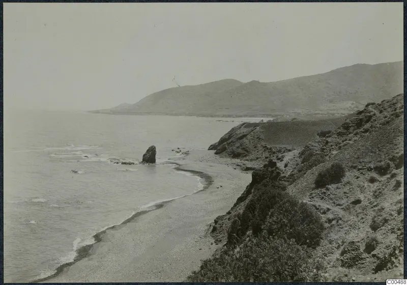 Coastline below the Kyrenia Mountains, with a sandy bay, a offshore rock stack and scrub-covered slopes.