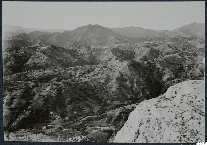 Wide view over hills and mountain ridges with terraced slopes, seen from a pale rocky outcrop in the foreground.