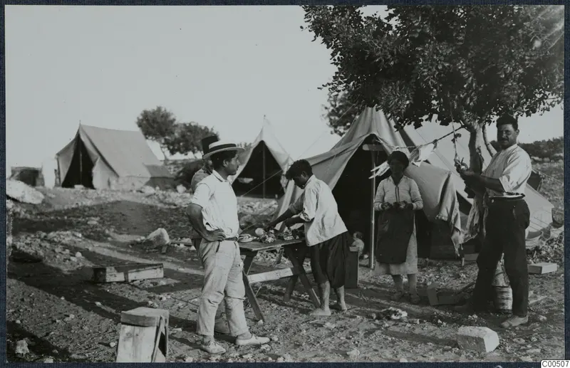 Camp tents and five people beside a table with food and plates at Vouni, under a tree