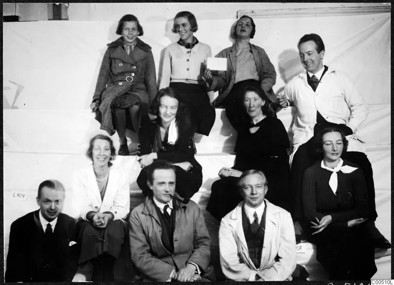 Group photograph of eleven people posed on white steps against a pale backdrop, including a girl, women and men.