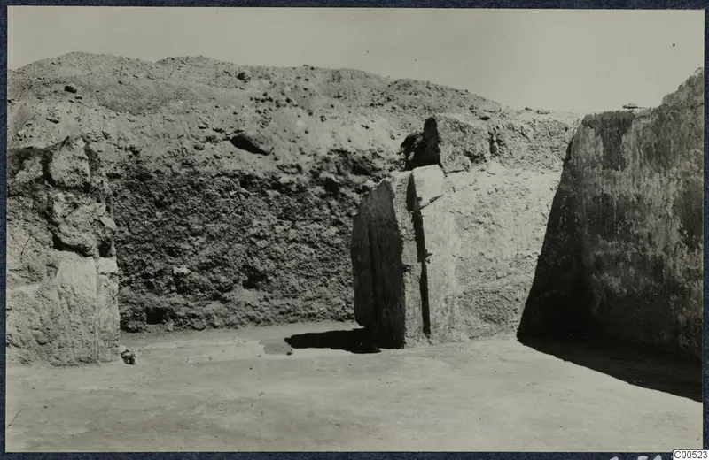 Large stone blocks and an upright stone slab in an excavation trench at Vouni, with an earth bank behind