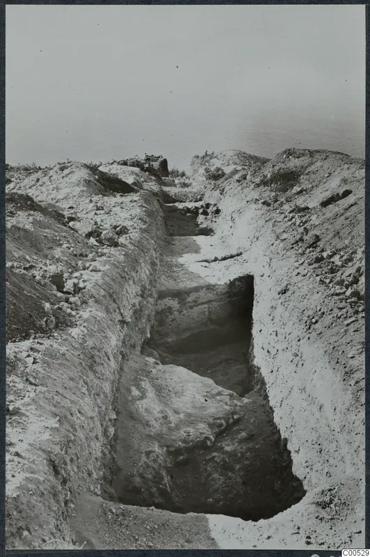 Excavation trench with loose stones along its banks at Vouni, with the sea visible in the background.
