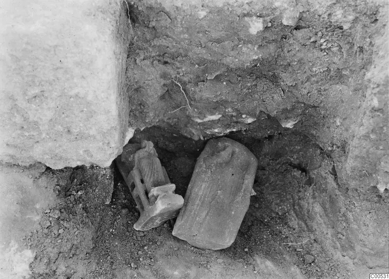 Finds in situ at Vouni Palace: a small figure and a rounded object lying in soil beside a large stone block.