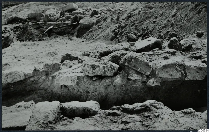 Excavation at the Temple of Athena, Vouni, with large stone blocks in a trench and a spade at the upper left