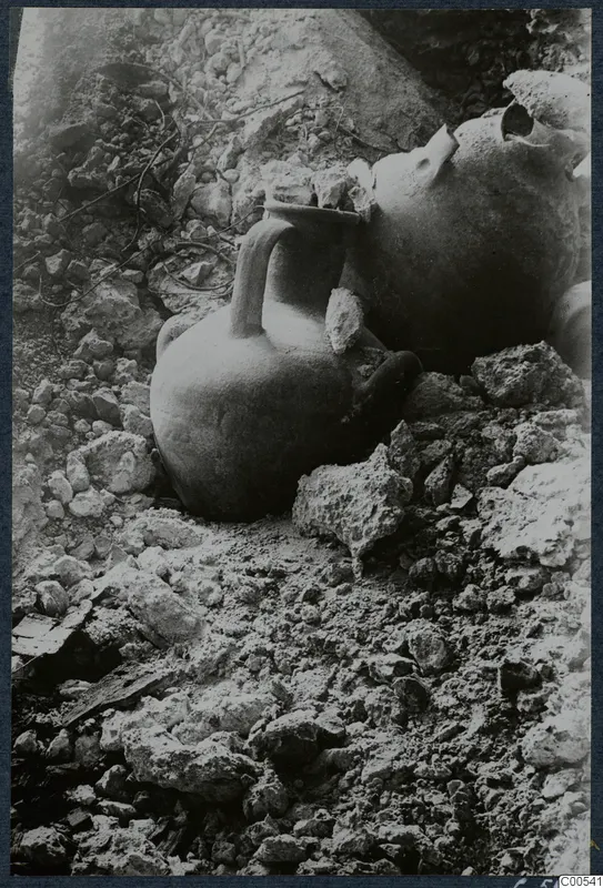 Two vessels lying among stones and rubble at Vouni, one a small jug with a strap handle.