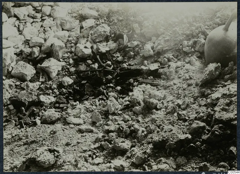 Loose stones and fragments on excavated ground at Vouni Palace, with a large vessel at the right edge