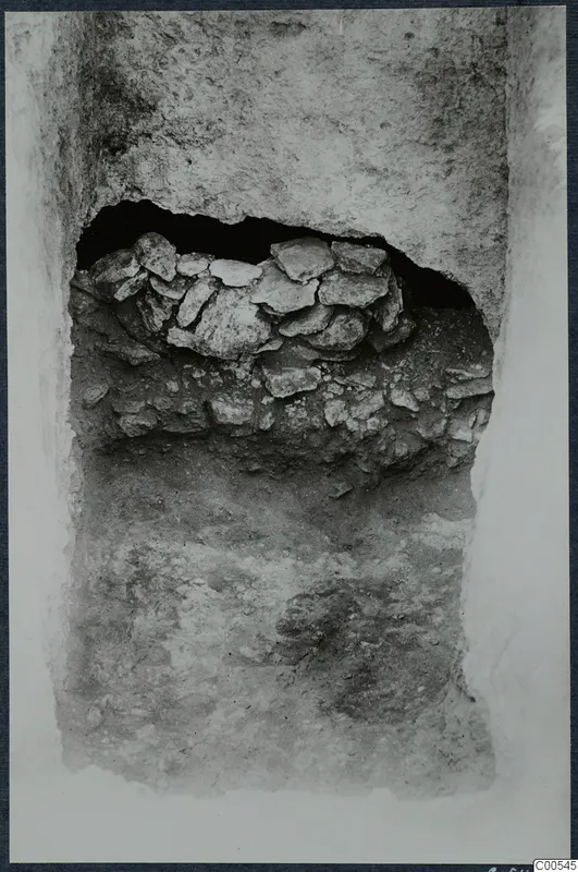 Excavated cutting with a heap of flat stones set into an opening in a soil face, at Vouni