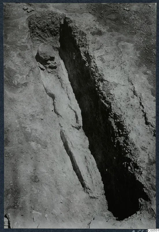 Narrow excavation trench at Vouni with a rounded stone and a line of stones along its edge