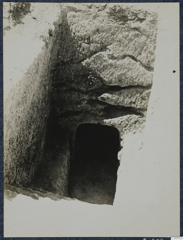 Cutting leading down to a dark rectangular doorway in layered rock at Vouni