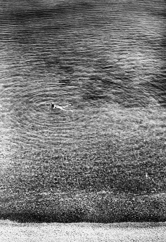 John Lindros swimming in the sea at Vouni, with rings spreading across the water above a stony beach