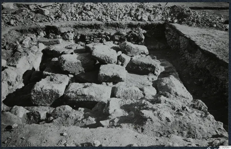 Excavated stone blocks and rubble at Vouni palace, with a trench and spoil heap behind.