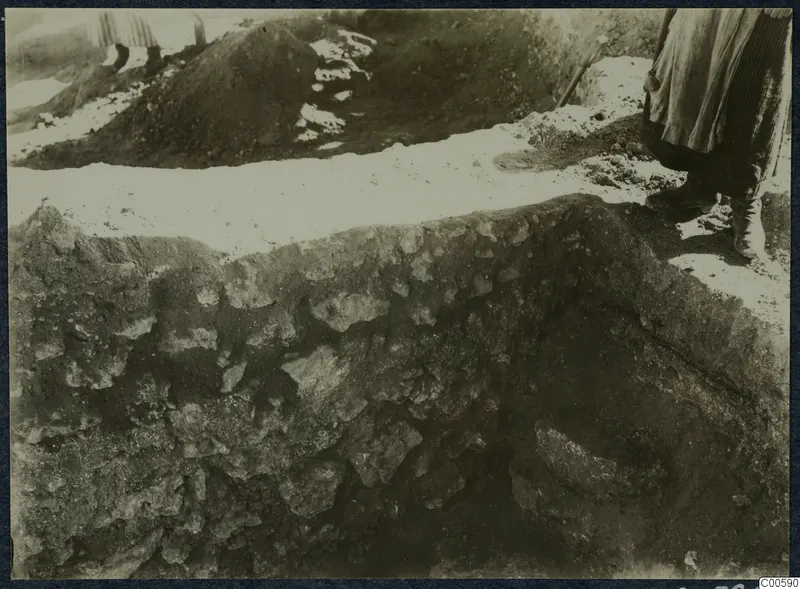 Excavation at Vouni palace: a person stands at the edge of a trench beside a cut face of stones and soil.