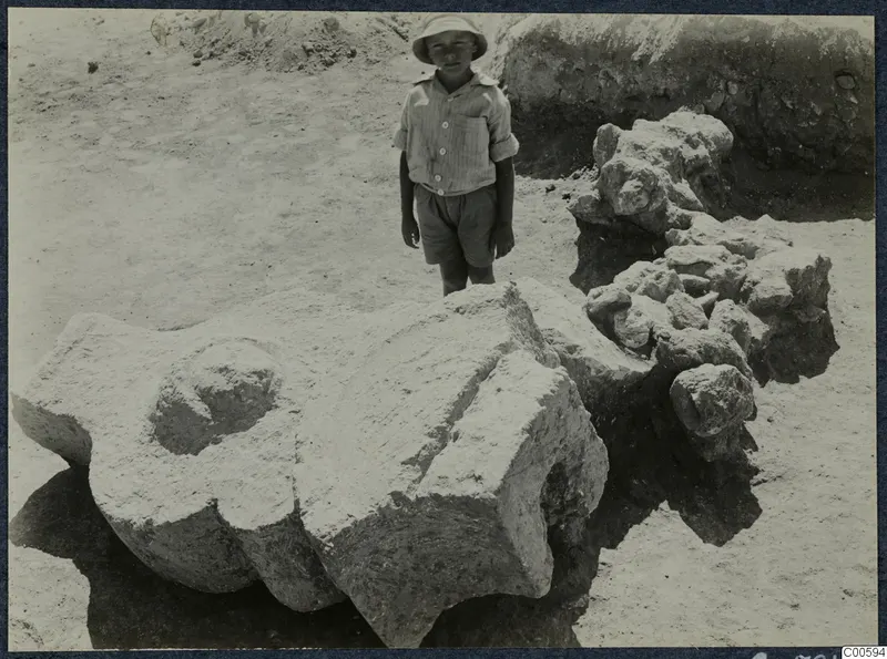 Boy in a wide-brimmed hat standing beside large worked stone blocks lying in situ at Vouni