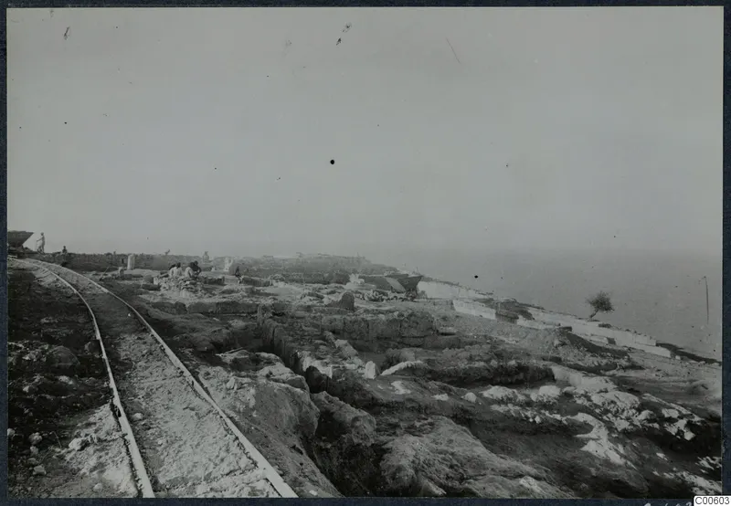 Excavation at the Vouni palace with a rail track running past trenches and cut stone walls toward the sea.
