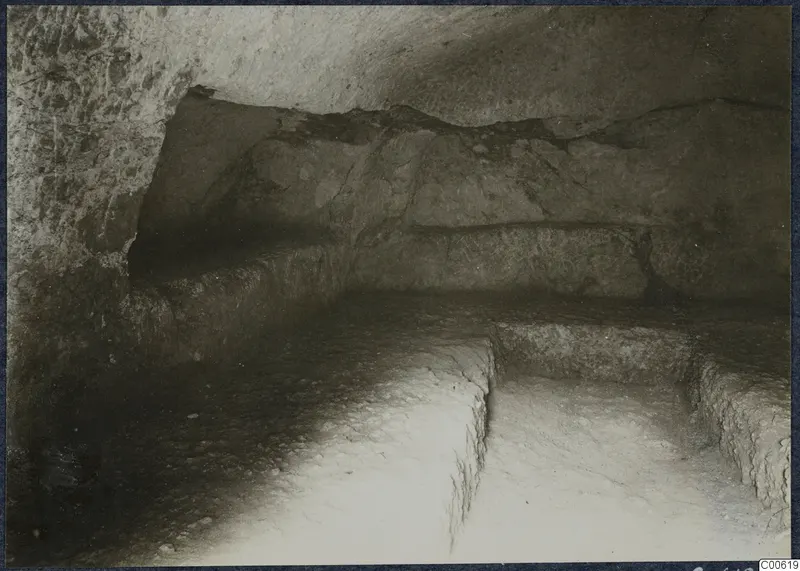 Interior of a rock-cut chamber at Vouni, with cut ledges along the walls and a stepped floor