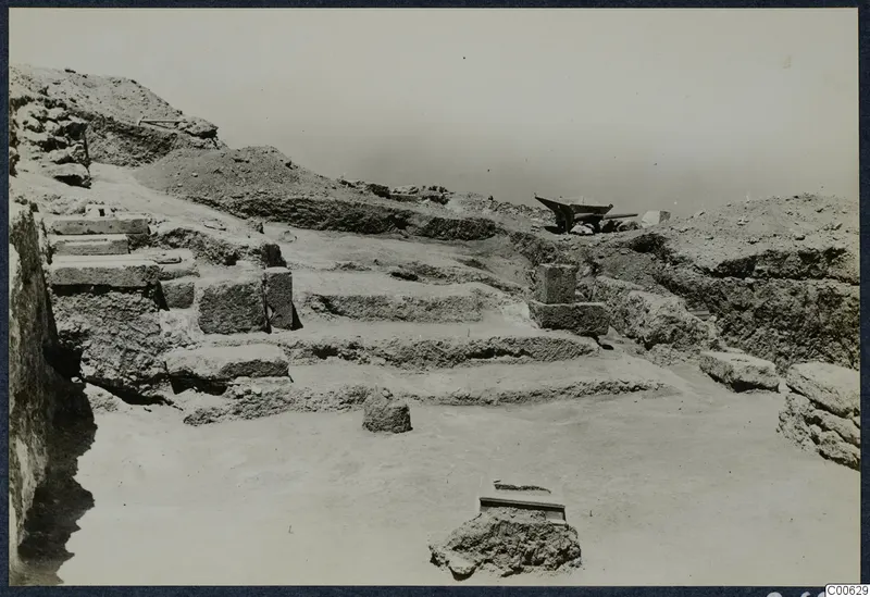 Stone steps cut into an excavated slope at Vouni Palace, with squared blocks and a wheelbarrow on the spoil heap above