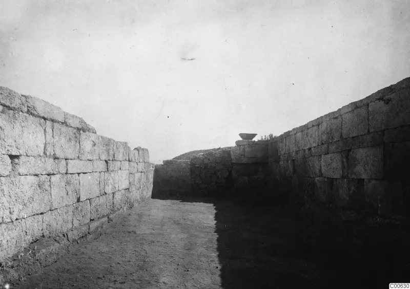 Excavated passage between tall ashlar walls at Vouni Palace, with a shallow bowl on top of a wall block.
