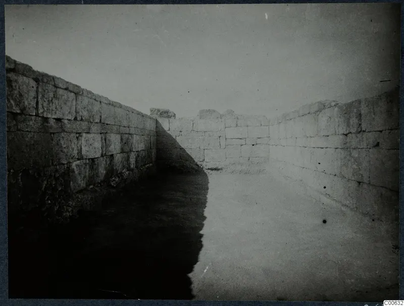Ashlar stone walls of a narrow passage or room at Vouni, with a paved or cleared floor between them.