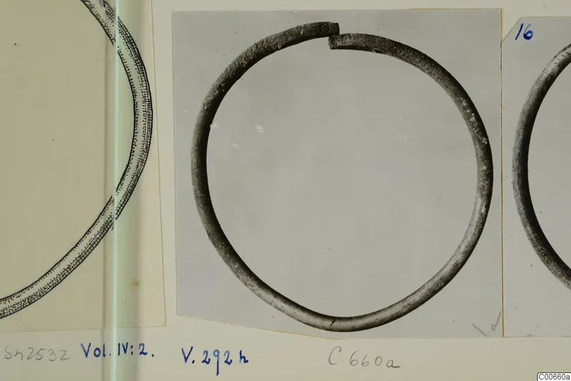 Silver bracelet, an open ring with a gap at the top, photographed on a grey card mount beside other drawings and photographs.