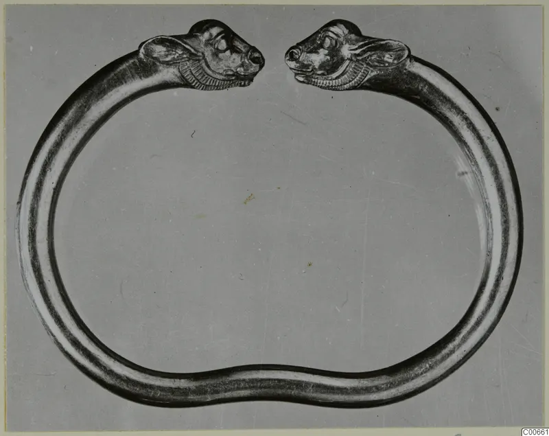 Gold bracelet with an animal head at each open end, photographed against a grey backdrop