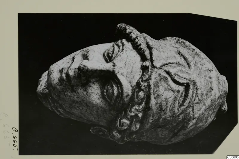 Limestone head of Athena wearing a helmet, shown lying on its side against a dark background.
