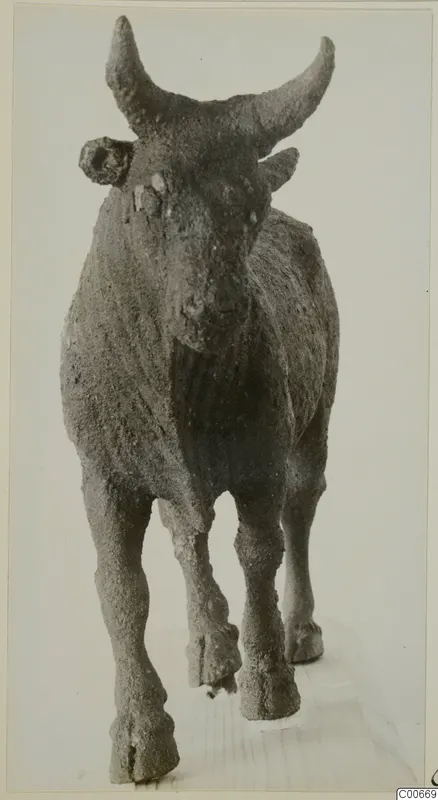 Bronze statuette of a horned animal, perhaps a bull, standing on a wooden board.