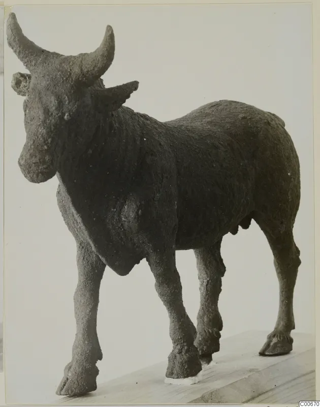 Bronze figure of a bull with long curved horns, standing on a wooden base and seen obliquely from the front.