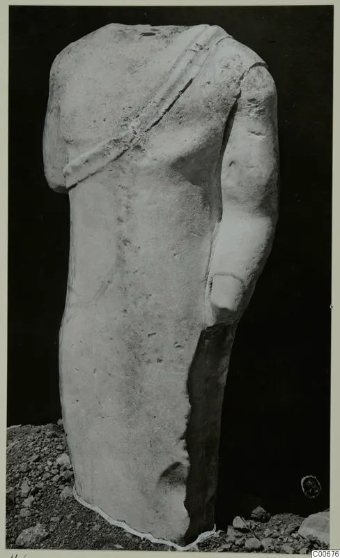 Headless limestone statue torso from Vouni with a band across the chest, standing on gravel.
