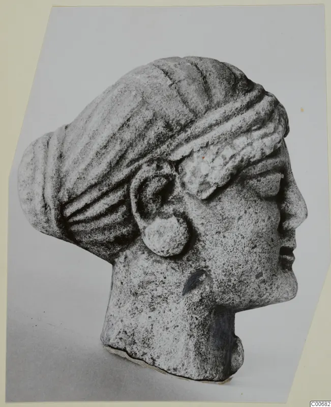 Limestone head in right-facing profile, hair drawn back in ridged bands into a bun, with a large disc earring, from Vouni