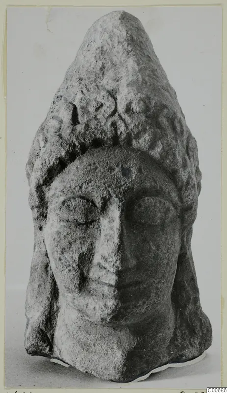 Limestone head with a tall conical headdress, from Vouni, shown frontally against a plain grey background