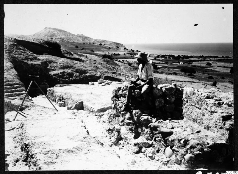Alfred Westholm seated on a stone wall of the theatre at Soli, with hills, fields and the sea behind.