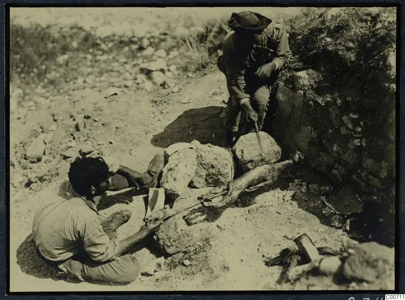 Two men roasting meat on a spit over stones at Soli