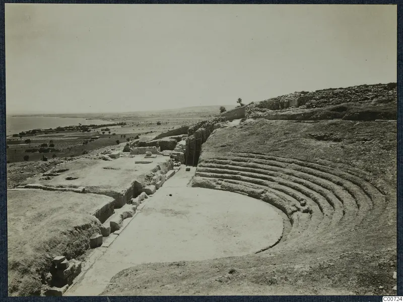 Theatre ruins at Soli with curved rows of stone seating, looking across the flat ground toward the sea and plain.