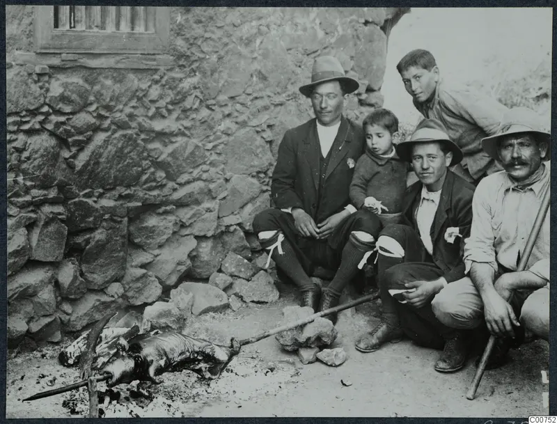 Five people sit by a stone wall beside a whole animal roasting on a spit over a fire at Galini.