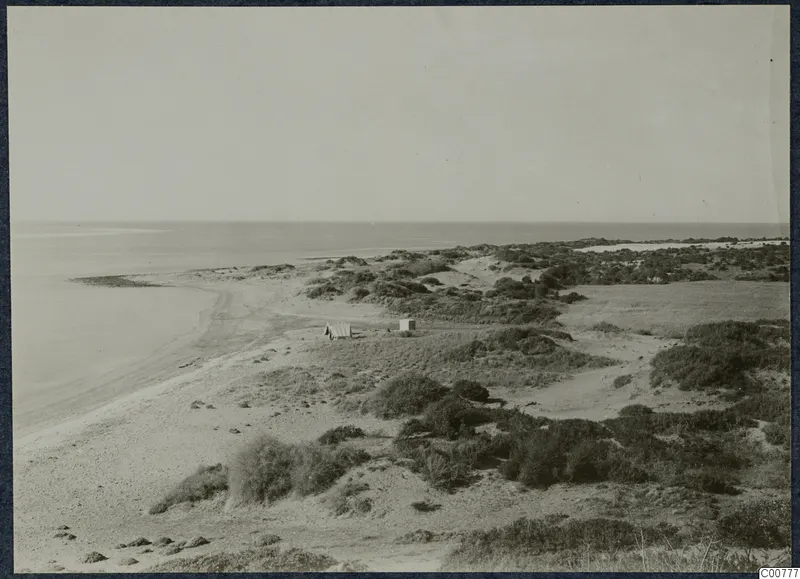 Landscape at Oura: a sandy coast with dunes and low scrub, a pale tent and a small hut, with the sea beyond.