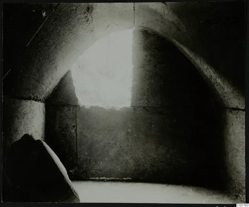 Interior of tomb T.1 at Trachonas, showing an arched stone chamber lit through an opening in the back wall.