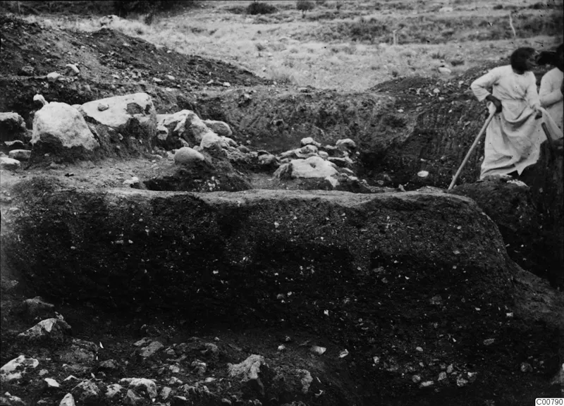Excavation trench at Plakes, Lapithos, with pale stones in the cut and two people at the right edge