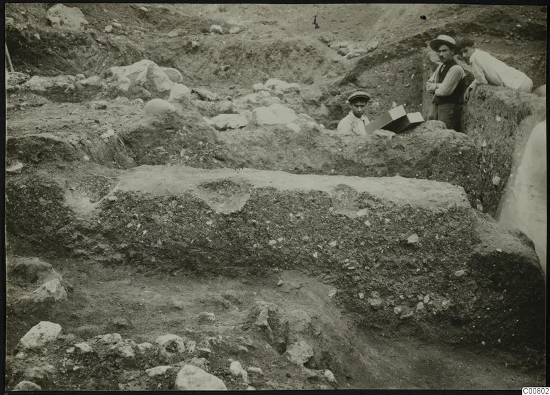 Cross-section of the Plakes E.C. house excavation at Lapithos, with three people at the trench edge.