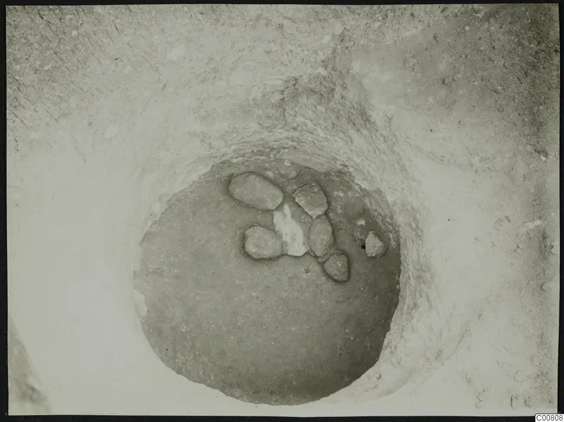 Excavation at Plakes, Lapithos: stones lying in a round pit seen from above, with a pale patch among them.