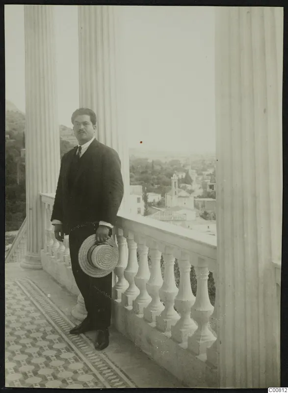Perikles Kaplanis, mayor of Lapithos, standing with a straw hat on a columned balcony above the town