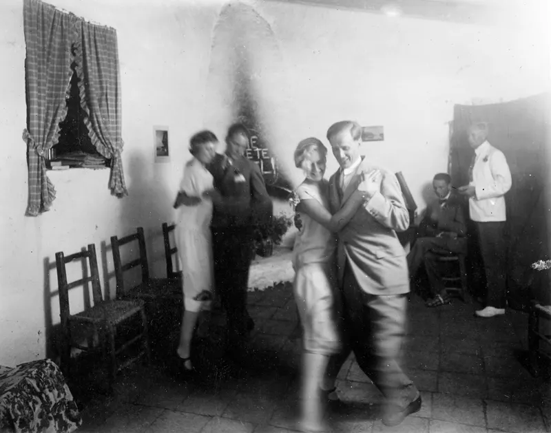 Dancing couple in a whitewashed room at Machairas, with other people standing and seated along the walls.