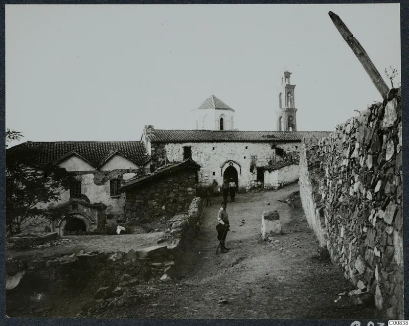 Monastery at Machairas seen from a dirt track, with whitewashed walls, tiled roofs, a bell tower and three people