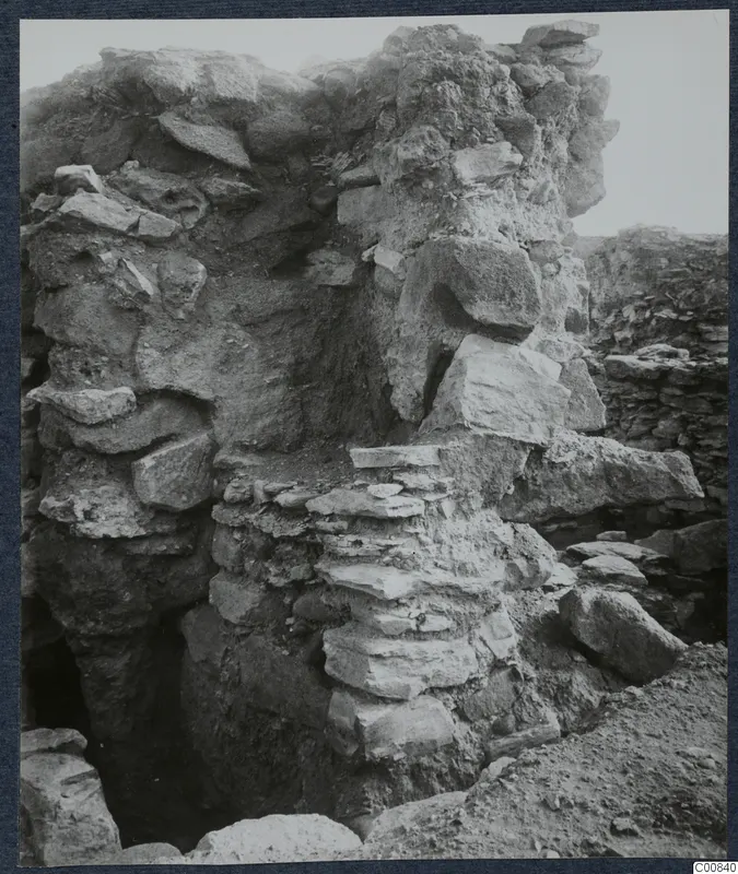 Standing wall of rough stone blocks at the Idalion acropolis excavation, with fallen stones and soil at its base.