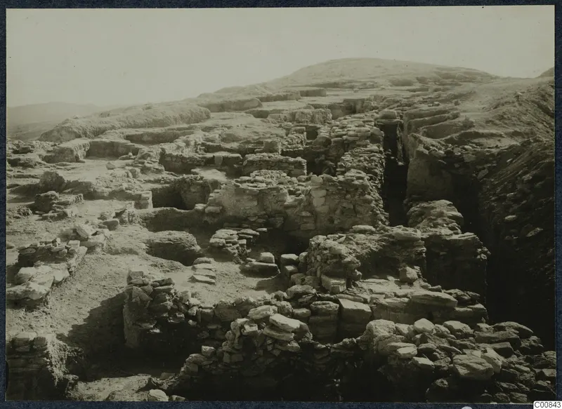 Excavated stone walls and foundations on the Idalion acropolis, with a deep cutting on the right and a hill behind.