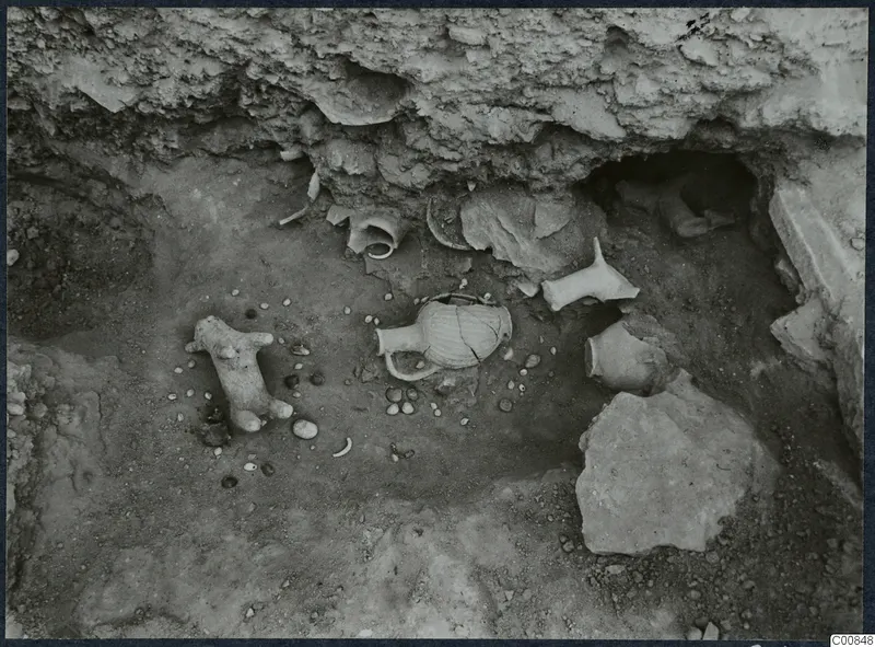 Excavated pit at Idalion Acropolis with pottery vessels, a small animal-shaped vessel and scattered stones on the floor