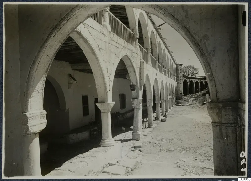 Monastery courtyard at Lambousa, seen along a stone arcade of pointed arches with a balcony on the upper storey