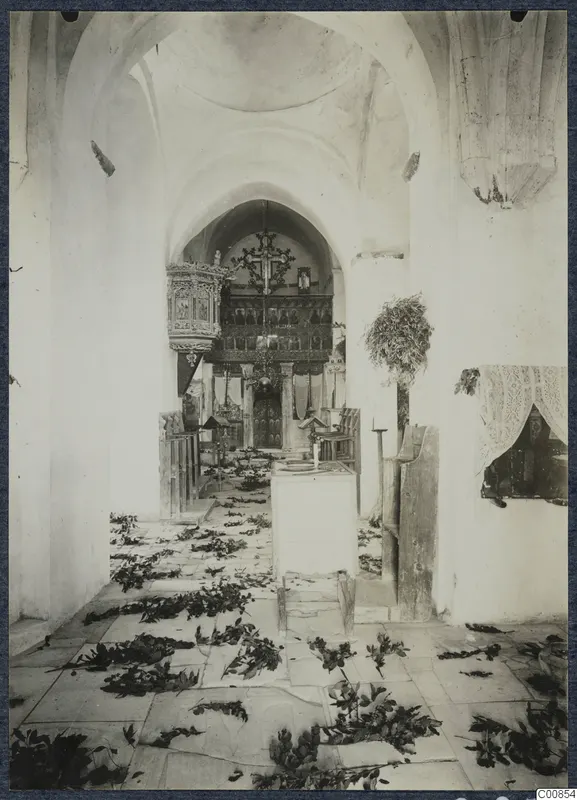 Interior of the monastery church at Lambousa, with leafy branches scattered over the stone floor and an icon screen at the far end