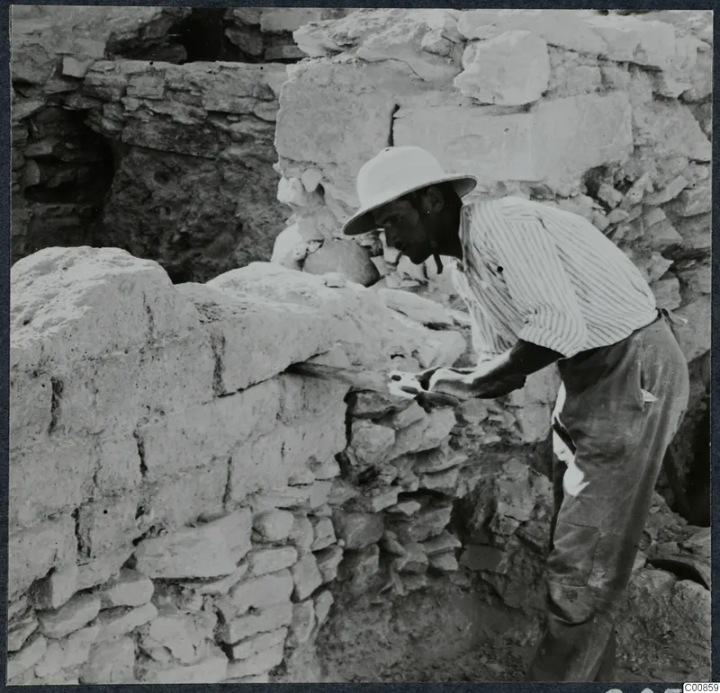 Man in a pith helmet sawing a mud-brick wall at Idalion during excavation